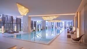 A modern indoor pool area with geometric lighting fixtures, lounge chairs, and a glass-enclosed pool. - Grand Hyatt Xi An (Xi'an)