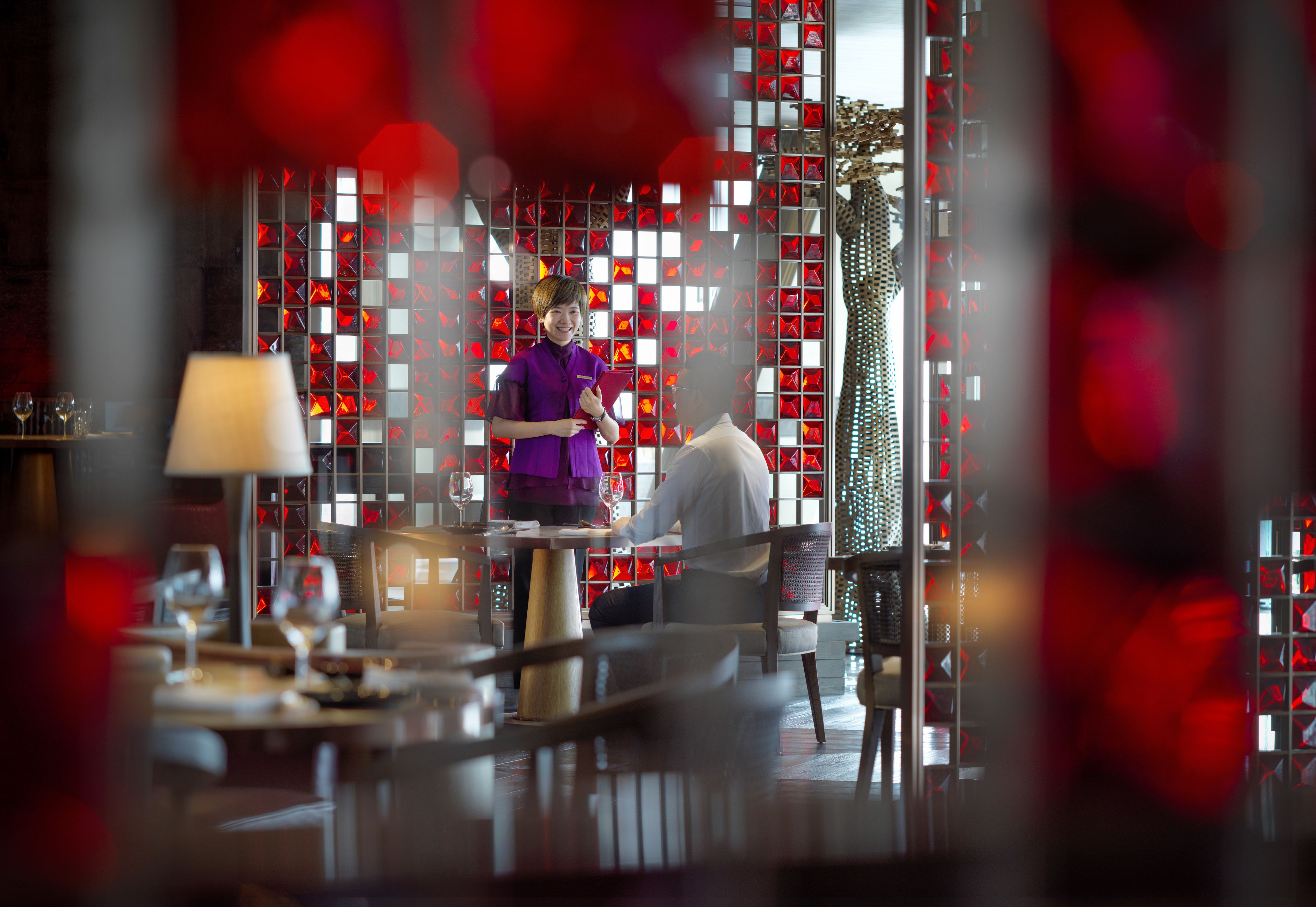 A restaurant with a modern interior, featuring a patterned glass wall and a person seated at a table.