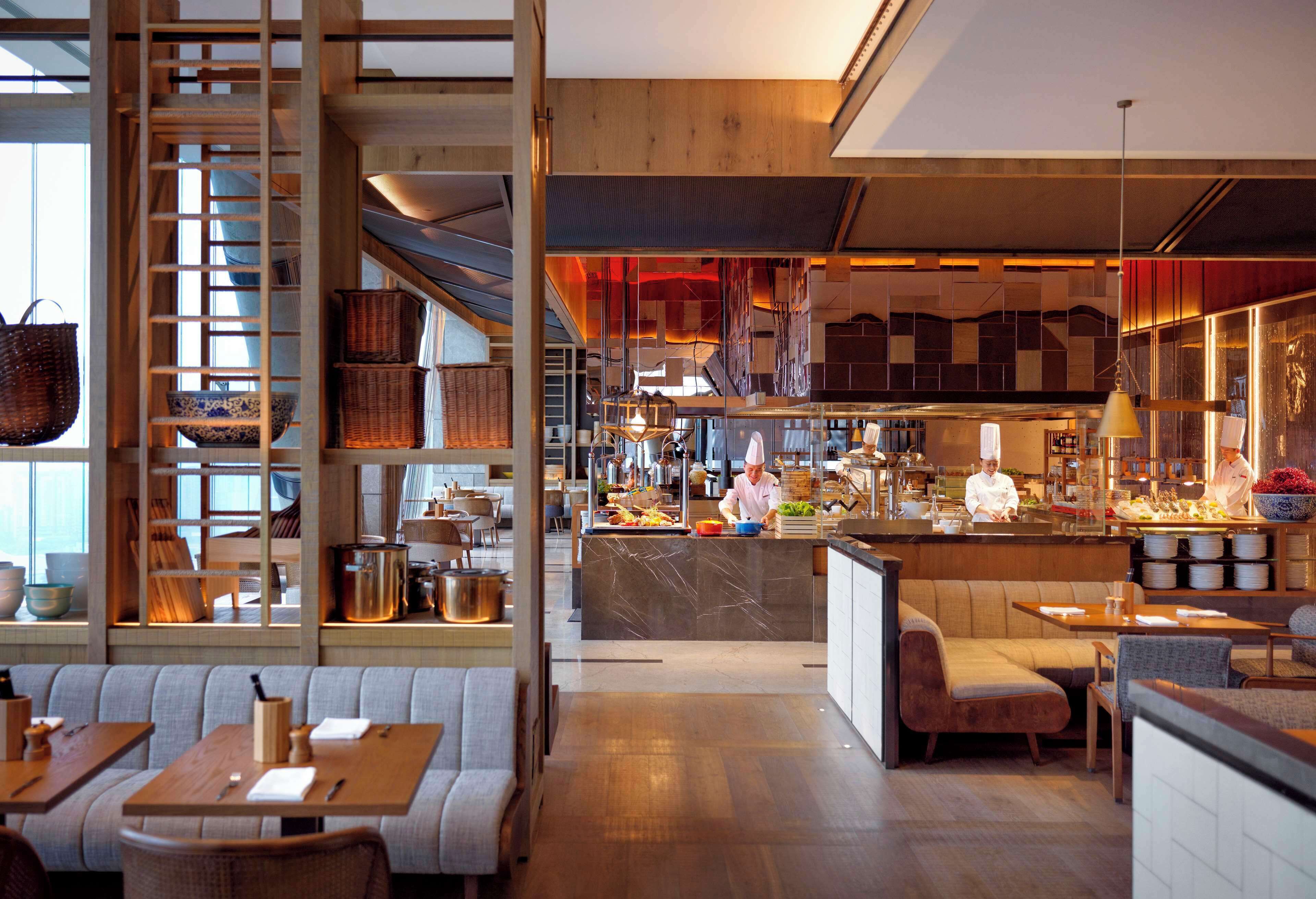 A modern restaurant interior with wooden accents, a central bar area, and seating arrangements.
