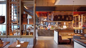 A modern restaurant interior with wooden accents, a central bar area, and seating arrangements.