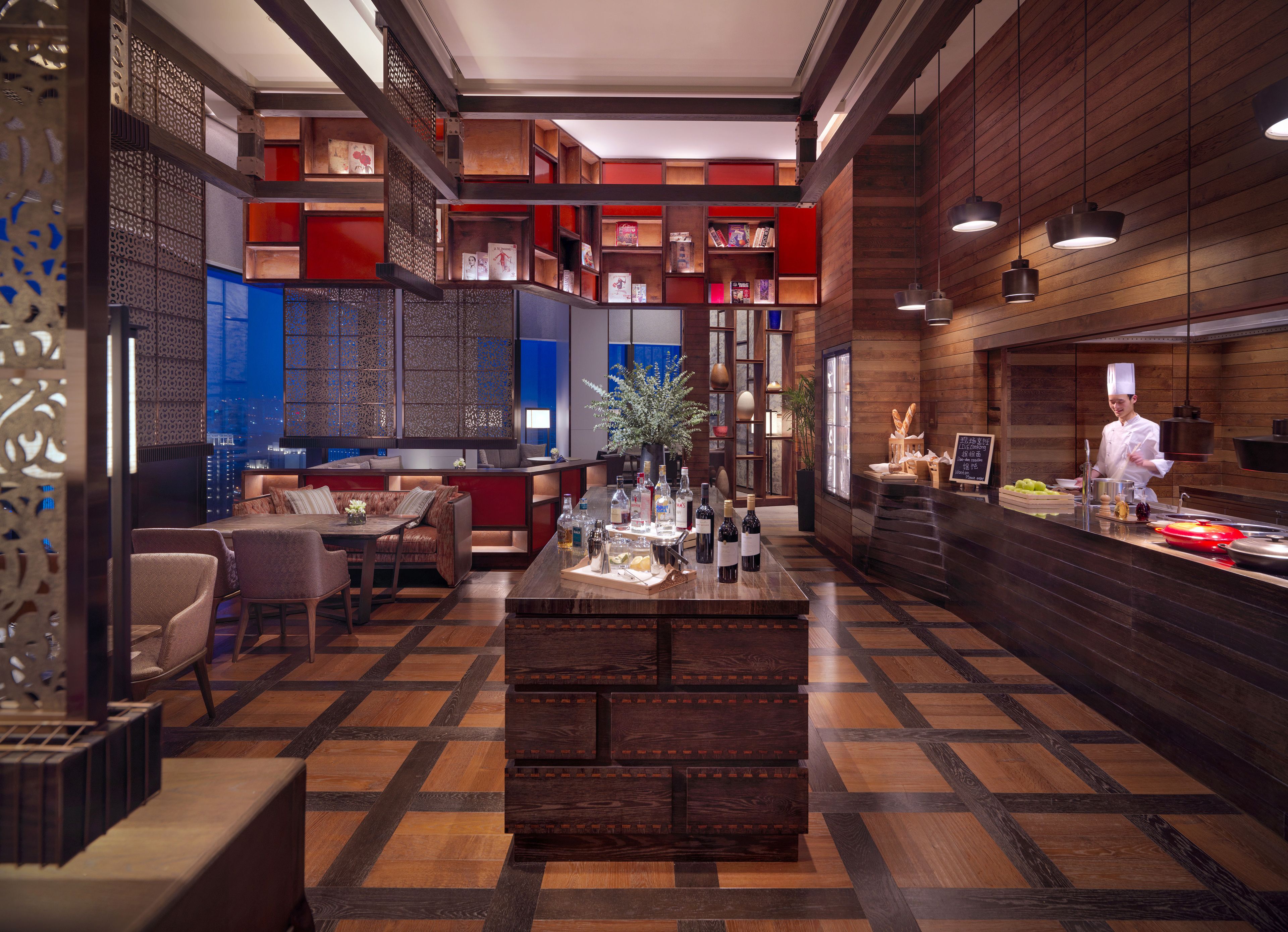 A modern hotel lobby with a central bar area, seating arrangements, and a view of the cityscape.