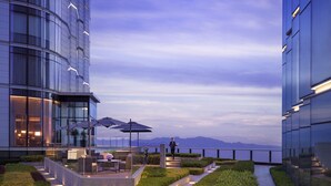 A modern building with a glass facade, outdoor seating area with umbrellas, and a landscaped garden. - Grand Hyatt Xi An (Xi'an)