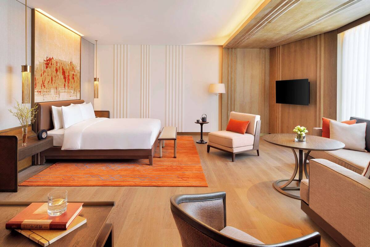 A modern hotel room with a large bed, a sofa, a round coffee table, and a TV mounted on the wall.