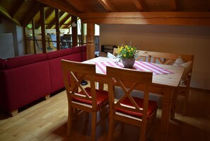 Une table de salle à manger en bois, un canapé rouge et des chaises en bois, le tout dans une pièce dotée d’un plafond en pente et de grandes fenêtres.