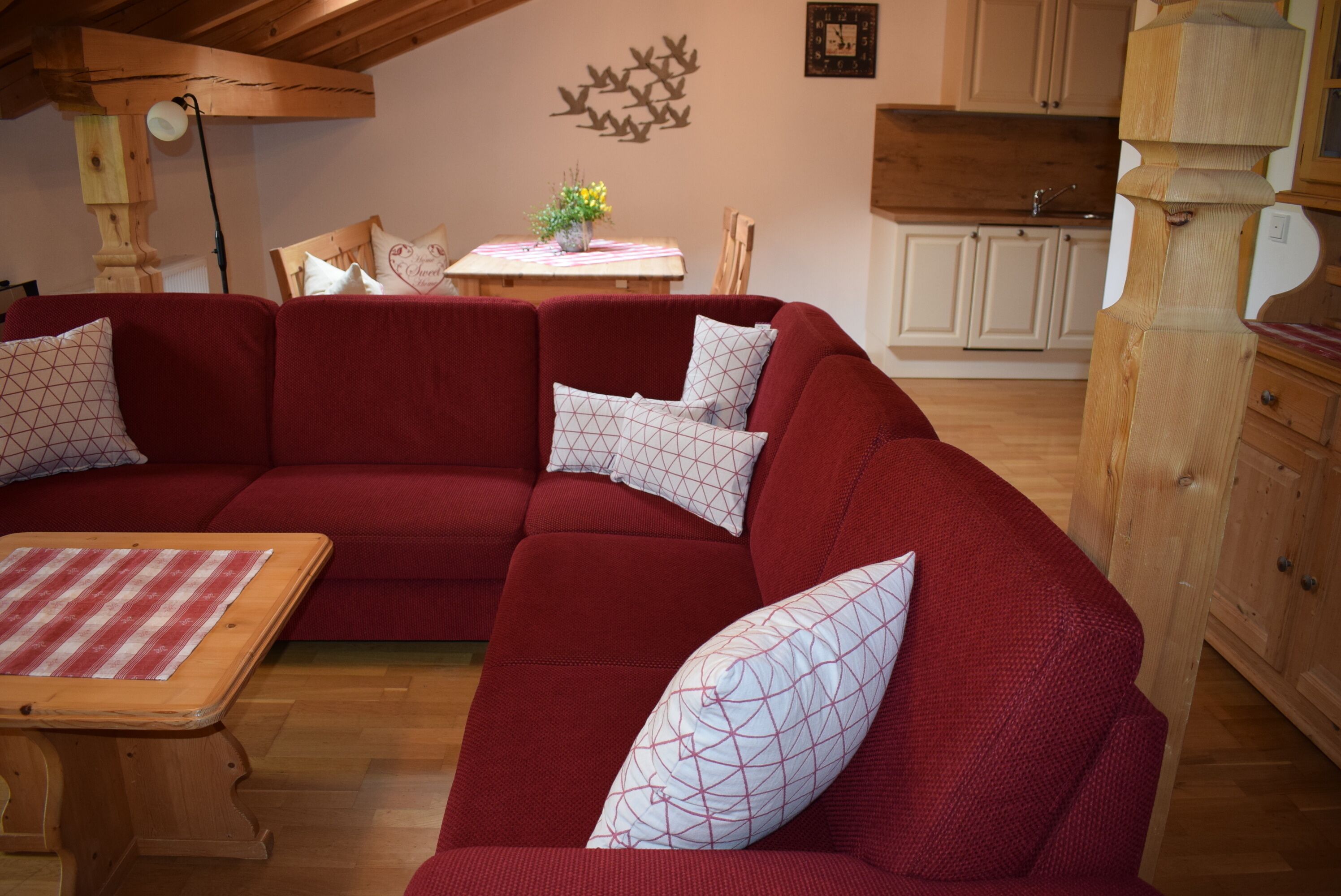 A red sectional sofa with patterned pillows, a wooden coffee table, and a dining area with a table and chairs.