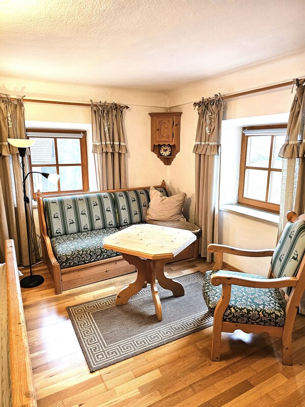 A cozy room with a wooden floor, a patterned sofa, a wooden table, a chair, and a wall clock.