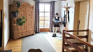 A rustic room with wooden floors, a wooden bench, a wooden table, a plaid-curtained window, and a wooden cabinet with hanging plants.