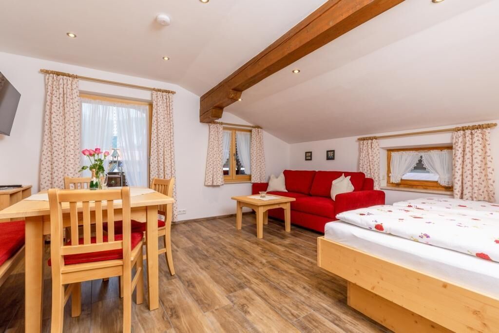 A cozy room with a wooden dining table, red sofa, and a bed with floral bedding.