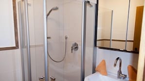 A glass-enclosed shower with a handheld showerhead and a handheld faucet.