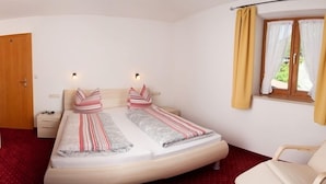 A double bed with striped bedding, a bedside table, a chair, a window with curtains, and a door.