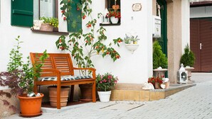 A white building with green shutters, a wooden bench, and various potted plants.