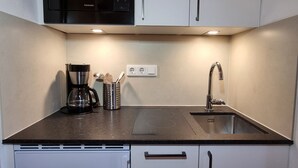 Een kleine keuken met een magnetron, koffiezetapparaat en bestek op het aanrecht, een spoelbak en een vaatwasser eronder.