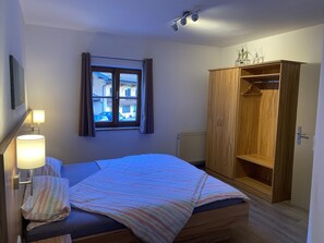 A bedroom with a bed, a window with curtains, a wooden wardrobe, and a radiator. - Ferienwohnung 1 (65qm), 2 Schlafzimmer, Balkon, Kochnische, WLAN, max 4 Personen (Ruhpolding)