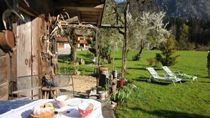 Una cabaña de madera rústica con una mesa de comedor al aire libre, rodeada de vegetación y vistas a una ladera.
