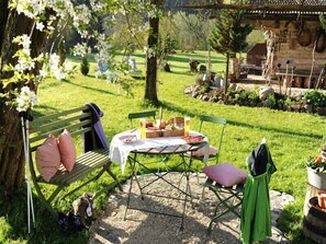 A picnic setup with a table, chairs, and a bench in a grassy outdoor area with trees and a building in the background. - Ferienwohnung 1 (65qm), 2 Schlafzimmer, Balkon, Kochnische, WLAN, max 4 Personen (Ruhpolding)