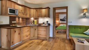 Cocina compacta con gabinetes de madera, microondas y cafetera. En el área de estar contigua, hay un sofá verde.