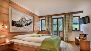 Un dormitorio con cama de madera, televisor montado y un ventanal con cortinas.