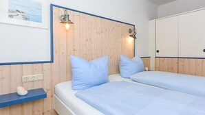 Et soveværelse med to senge, træpaneler på væggene, en hylde med en lampe og et indrammet billede.