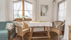 Ein gemütliches Zimmer mit einem petrolfarbenen Sofa, zwei Korbstühlen, einem kleinen Tisch mit einer Schale und einem Spiegel an der Wand.