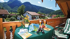A balcony with a view of a village and mountains, a table with books and binoculars, and a wooden railing. - Ferienwohnung 4, 2 Personen, 50 qm., 1 Schlafzimmer, DU/WC, TV, Zimmersafe, Balkon (Oberwössen)