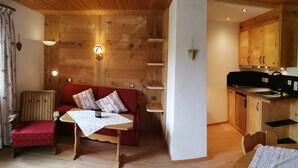 A cozy cabin interior with a wooden interior, a red sofa, a small table, and a kitchenette area. - Morgensonne one-room app. 28sqm, shower/WC, kitchenette, balcony (Reit im Winkl)