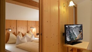 Quarto com painéis de madeira, uma cama, almofadas, uma televisão sobre uma mesa de madeira e luminárias fixadas na parede.