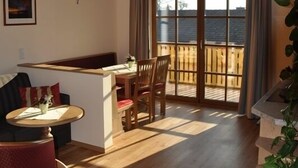 Une pièce chaleureuse avec un plafond en bois, une table à manger avec des chaises, un petit coin cuisine et une porte-fenêtre coulissante donnant sur un balcon.