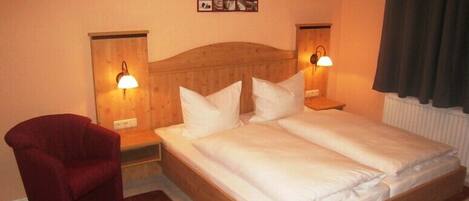A hotel room with a wooden bed, two bedside lamps, a red chair, and a wall-mounted picture.