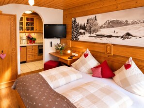 A hotel room with a bed, a TV, a painting of a snowy landscape, and a kitchen area.