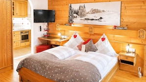 Ein Hotelzimmer mit Holzvertäfelung, einem Bett mit gemusterten Bettwaren, einem Schreibtisch mit Stuhl, einem Fernseher und einem Gemälde einer verschneiten Landschaft.