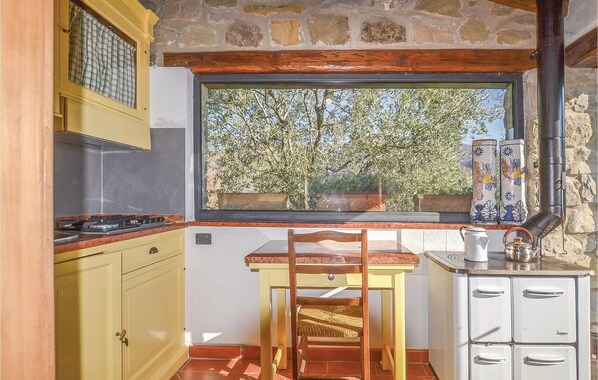 A kitchen with a window view of trees, a wooden chair, a stove, and a cabinet. - Cozy home in Bibbiena AR with private swimming pool, can be inside or outside (Bibbiena AR)