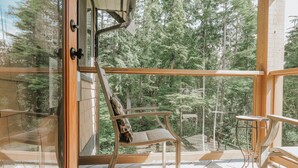 Eine Holzterrasse mit einer Glastür, die zu einem bewaldeten Gebiet führt.
