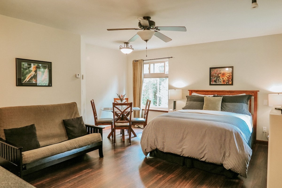 Quarto com cama, sofá, mesa de jantar com cadeiras, ventilador de teto e janela.
