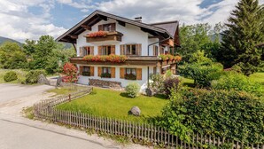 A two-story chalet with wooden balconies, a stone foundation, and a well-maintained garden.