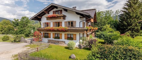 A two-story chalet with wooden balconies, a stone foundation, and a well-maintained garden.