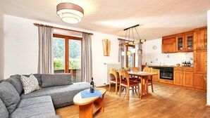 A modern living room with a sofa, a dining table with chairs, and a kitchen area with wooden cabinets and a stove.