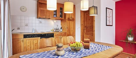 A modern kitchen with wooden cabinets, a dining table with a blue patterned tablecloth, and a fruit bowl.