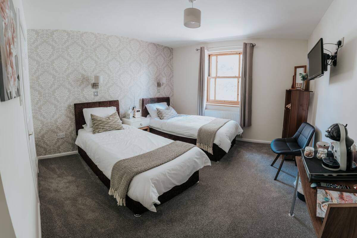 Une chambre d’hôtel avec deux lits, un bureau avec une chaise, une télévision et une fenêtre avec des rideaux.