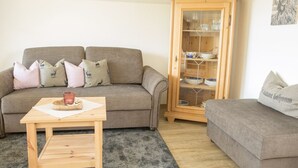 Ein Wohnzimmer mit grauem Sofa, einem Holzkasten und einem kleinen Tisch.