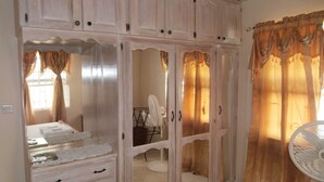 A bedroom with a large wardrobe, a bedside table, and a fan. - Sue'S Homestay (Oistins)
