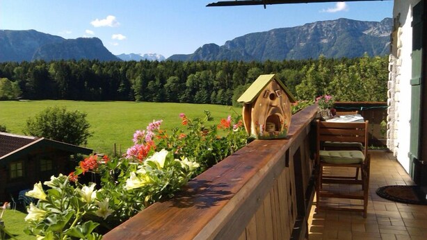 A wooden balcony with a wooden birdhouse, a table, and chairs. - Ferienwohnung Martina für 5 Personen, 3 Schlafzimmer mit Balkon, 90 m² (Inzell)