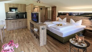 A bedroom with a bed, a TV, a wooden desk, and a kitchen area. - Double room no. 5, apartment, 1-2 persons, 40 sqm, west-facing balcony, W-LAN (Ramsau bei Berchtesgaden)