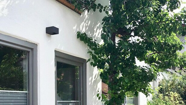 Een wit gebouw met grote ramen, een houten stoel en bloeiende plantenpotten.