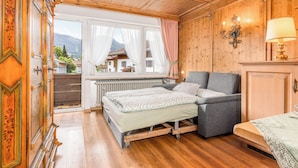 Une pièce comprenant un lit, un canapé, un radiateur, une fenêtre avec des rideaux et une vue sur une montagne.