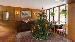 Une pièce chaleureuse avec un décor intérieur en bois, un sapin de Noël, une table à manger avec des chaises et une grande fenêtre ornée de plantes.