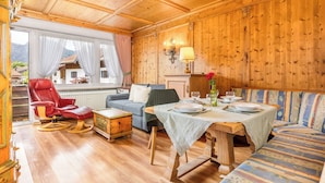 Une pièce aux murs lambrés, avec une table à manger dressée pour quatre personnes, un fauteuil en cuir rouge, un canapé et une vue sur une montagne par la fenêtre.