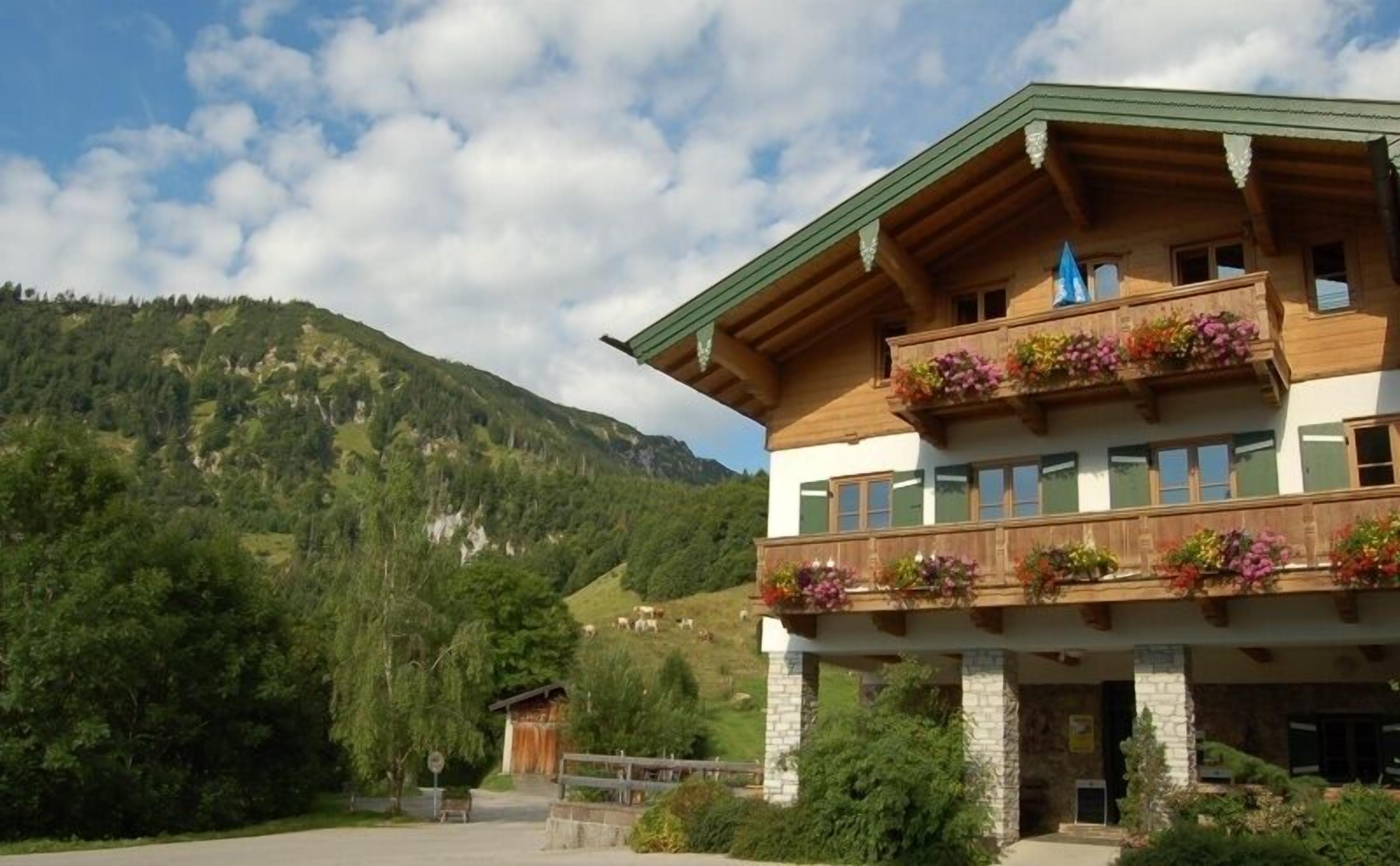 A two-story wooden building with balconies adorned with flowers, set against a mountainous backdrop.