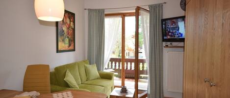 Una sala acogedora con una mesa de madera, un sofá verde y un televisor sobre un mueble de madera.