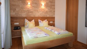 A double bed with floral bedding, a wooden headboard, and two wall-mounted lights. - 3. Fewo Hochlerch, 28 qm, 1-2 Pers., 1 Schlafzimmer, 1 Wohnküche, Süd-Balkon (Grassau)