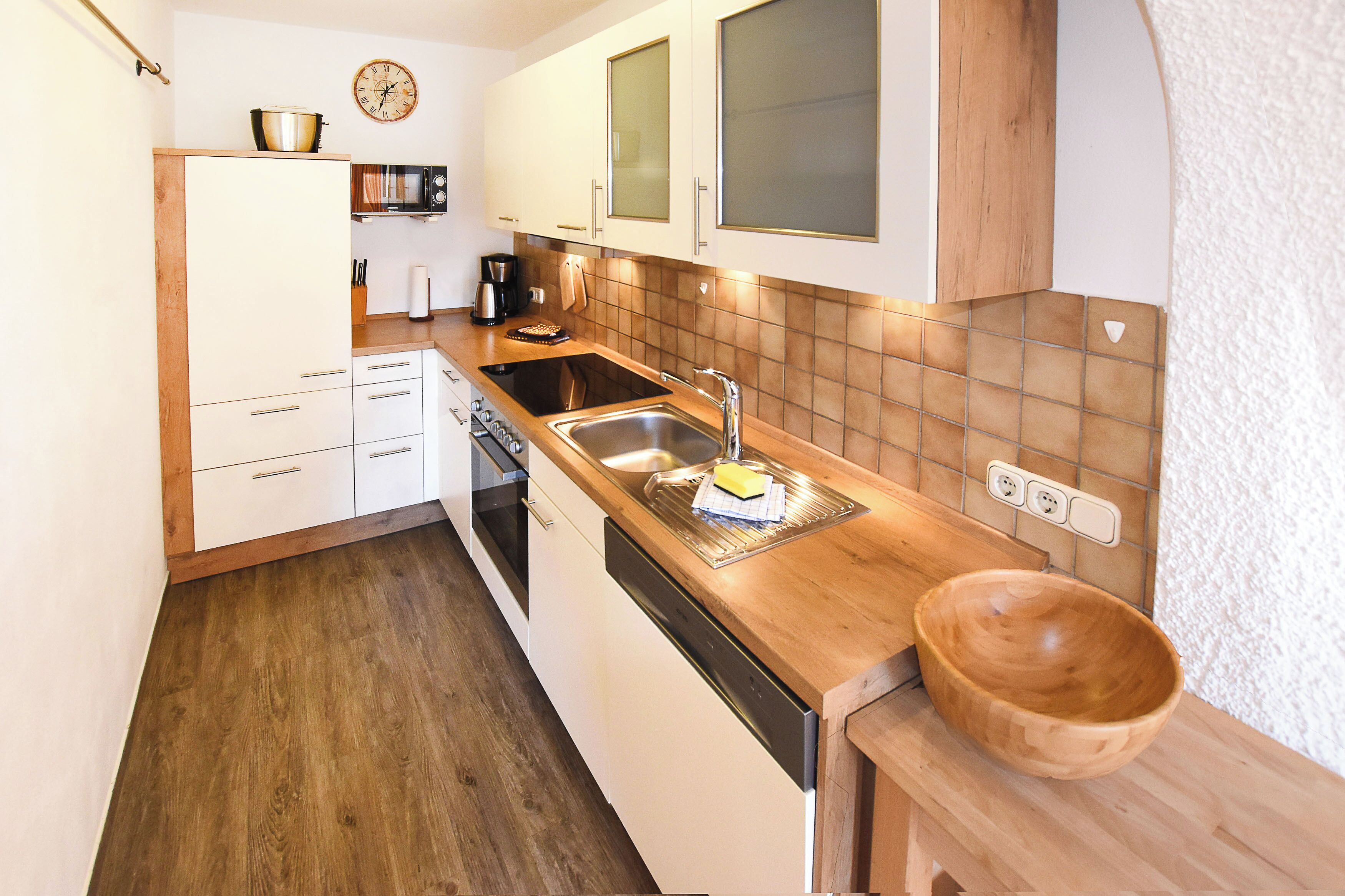 Une cuisine avec des meubles blancs, un plan de travail en bois, un évier, un four à micro-ondes et un saladier en bois.